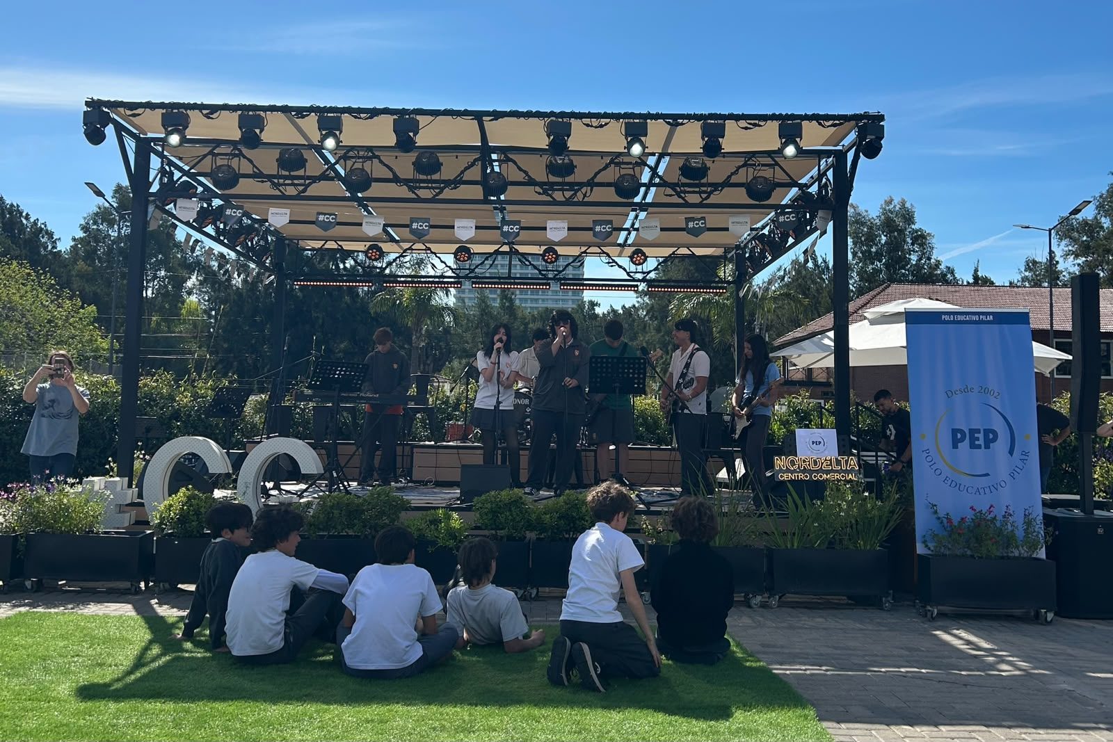 Banda de estudiantes tocando en el escenario al aire libre del Encuentro de Bandas 2026, con público sentado en el césped